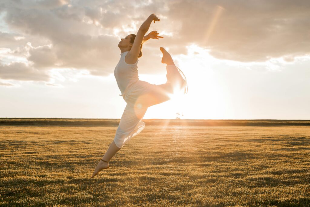 A ballet dancer showcasing elegance and flexibility in a sunlit grassy field during sunset.